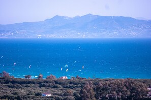 Un paisaje costero con vista al mar, windsurfistas y un skyline distante.