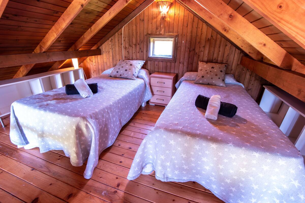 A cozy attic bedroom with two beds, a small window, and wooden beams.