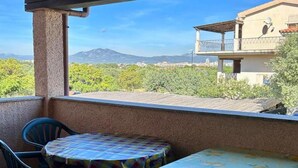 A balcony with a table and chairs, overlooking a mountainous landscape and a building with a balcony. - Olbia, Near Costa Smeralda Airport - Non-smoking (Olbia)