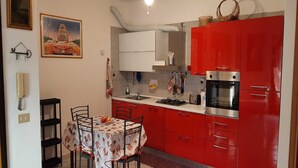 A compact kitchen with red cabinets, a gas stove, and a microwave. There is a dining table with chairs and a painting on the wall. - Olbia, Near Costa Smeralda Airport - Non-smoking (Olbia)