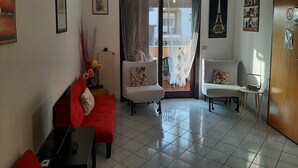 A living room with a red sofa, two white armchairs, a small table, and a balcony with a view. - Olbia, Near Costa Smeralda Airport - Non-smoking (Olbia)