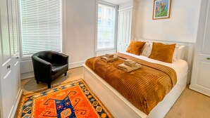 Quarto com cama, cadeira, tapete e um quadro na parede.