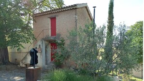 A rustic building with a red door, surrounded by greenery and a stone wall.