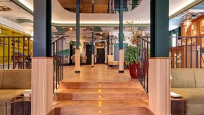 A spacious lobby with a wooden floor, green upholstered seating, and a staircase leading to upper levels.