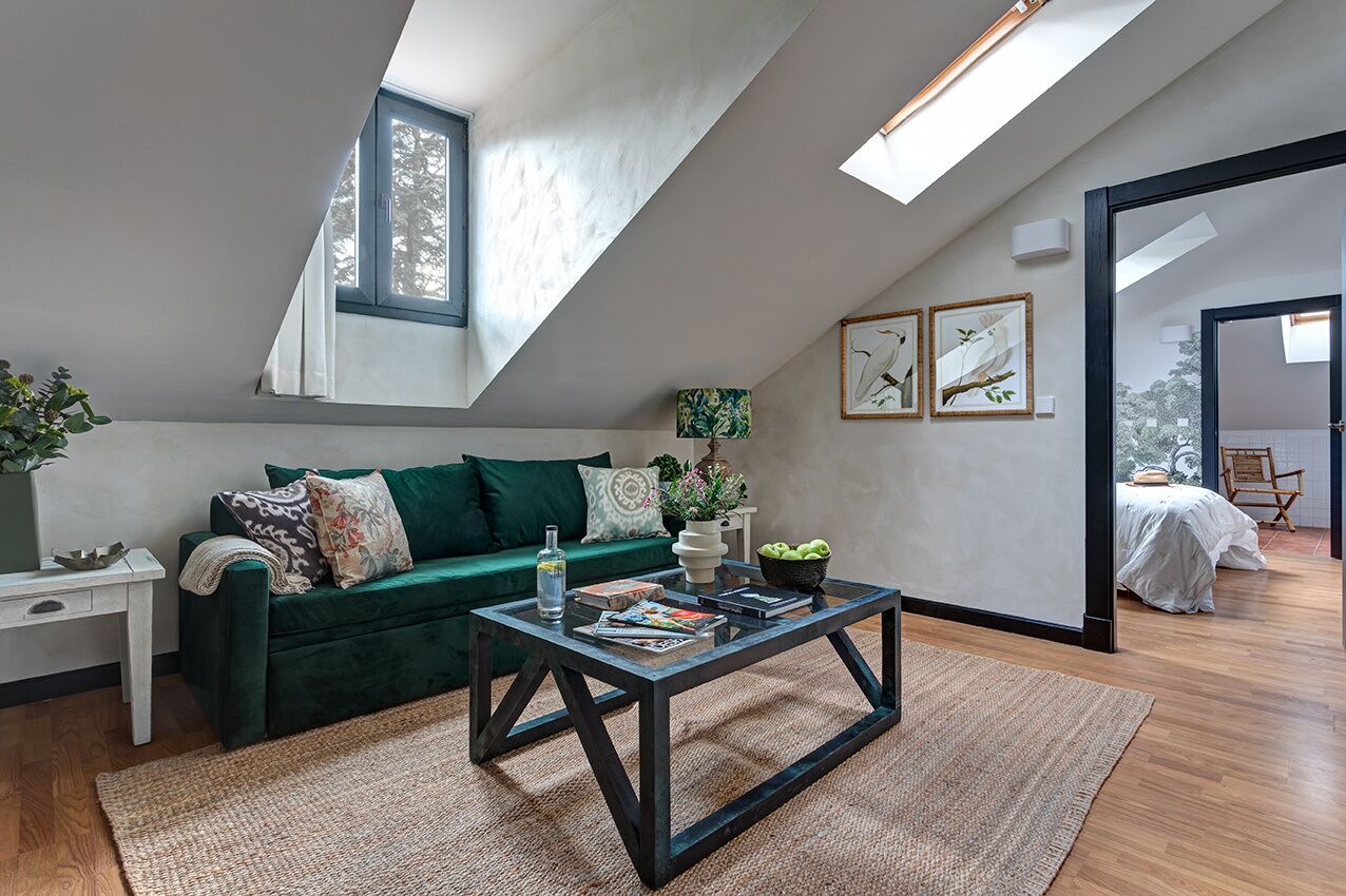 Une chambre de style loft moderne, avec un plafond en pente, un canapé vert, une table basse en bois et une vue sur l’extérieur.