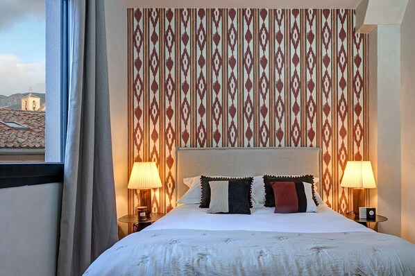 A hotel room with a large bed, two bedside lamps, and a patterned wallpaper.