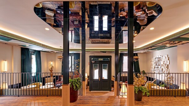 A spacious lobby with a wooden floor, a central staircase, and a decorative ceiling.