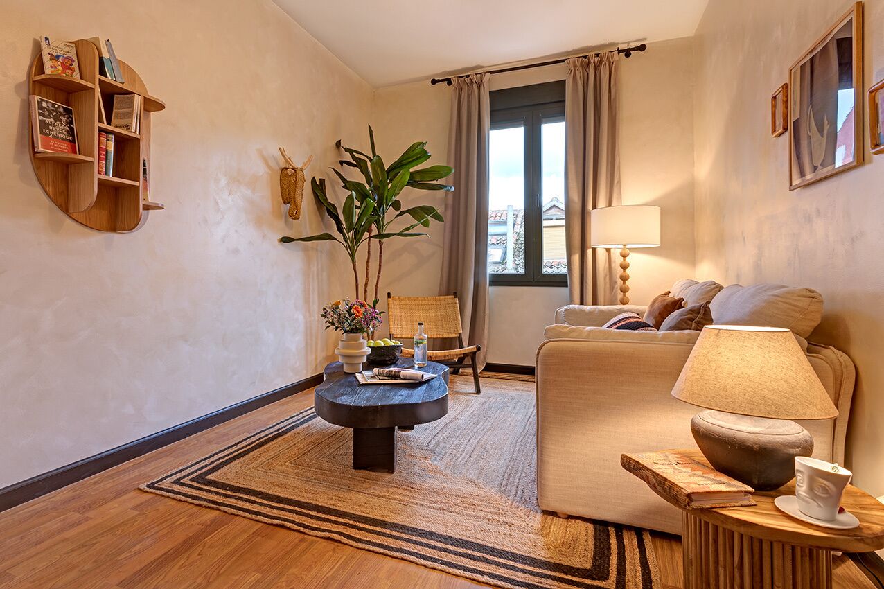 A cozy living room with a sofa, a coffee table, a bookshelf, and a window with curtains.