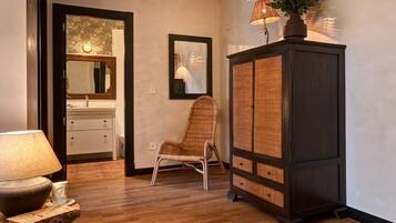 Una habitación con piso de madera, una silla de mimbre, un armario de madera oscura y un espejo con marco decorativo.