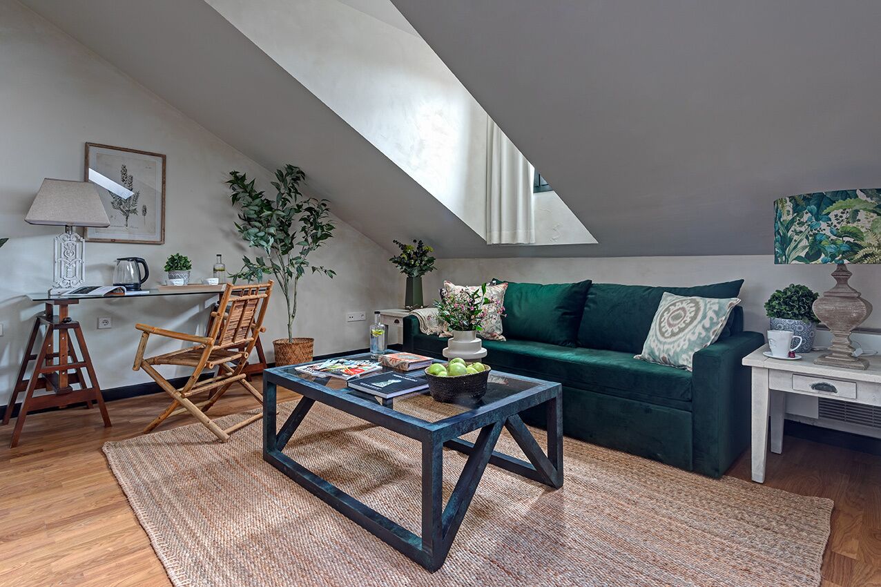 Een knus loft-woongedeelte met een donkergroene bank, een houten salontafel en een bureau met een lamp.