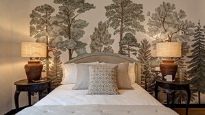 A bedroom with a bed, two nightstands, a headboard, and a wall mural of trees.