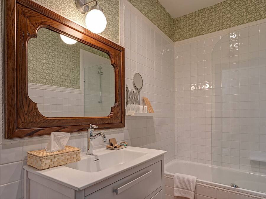 Un baño con un espejo de marco de madera, un lavabo blanco, una ducha con cerramiento de vidrio y un perchero para toallas.