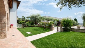 A well-maintained garden with a paved walkway, a brick building, and various trees and shrubs. - Casa Nicole (Manerba del Garda)