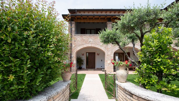 A brick building with a central entrance, surrounded by well-maintained hedges and potted plants. - Casa Nicole (Manerba del Garda)