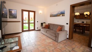 A living room with a sofa, a glass coffee table, and a door leading to a kitchen. - Casa Nicole (Manerba del Garda)