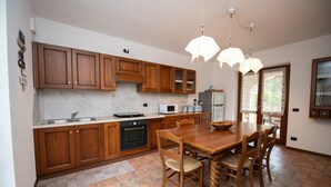 A kitchen with wooden cabinets, a dining table with chairs, a microwave, and a stove. - Casa Nicole (Manerba del Garda)