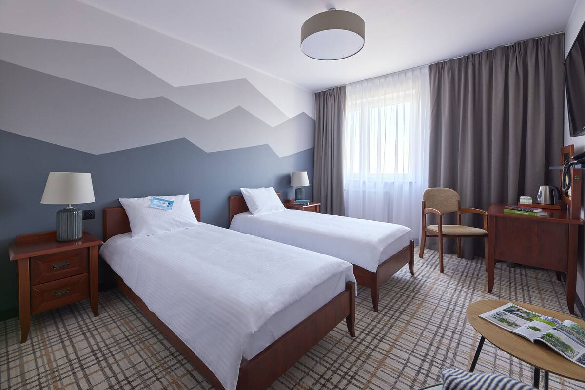 A hotel room with two beds, a desk, a chair, and a TV.