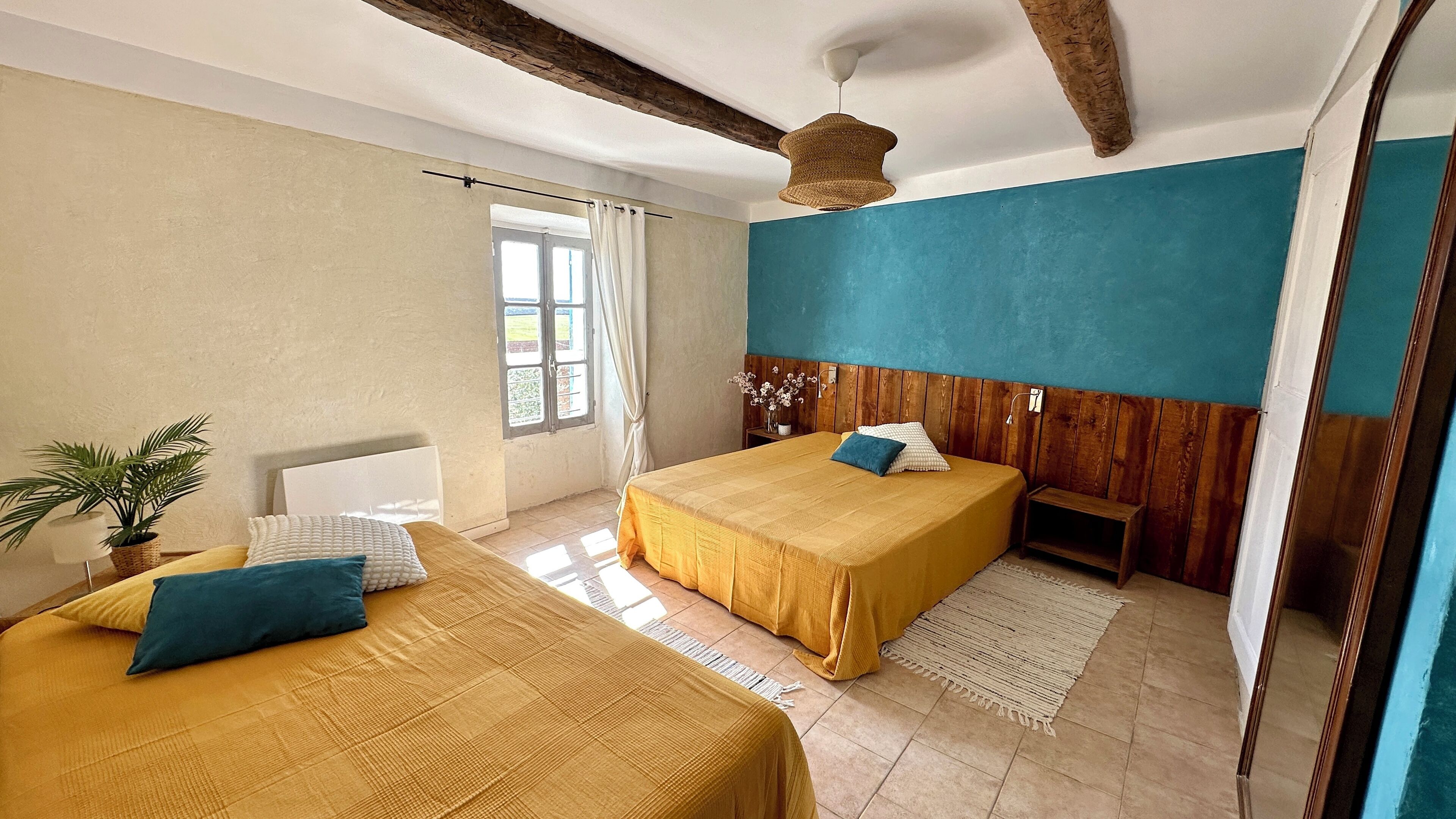 A bedroom with two beds, a wooden headboard, a hanging light fixture, and a window with curtains.