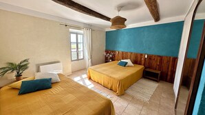 Un dormitorio con dos camas, cabeceros de madera, una lámpara colgante y un ventanal con cortinas.