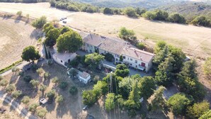Vista aérea de una amplia casa de dos pisos con techo de tejas, rodeada de árboles y campos abiertos.