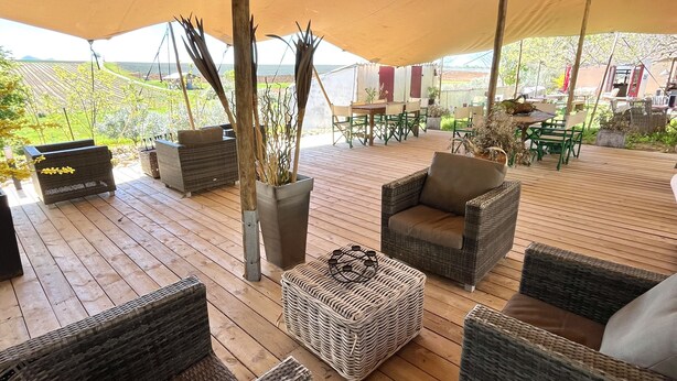 Un patio techado al aire libre con muebles de mimbre, una mesa y sillas.