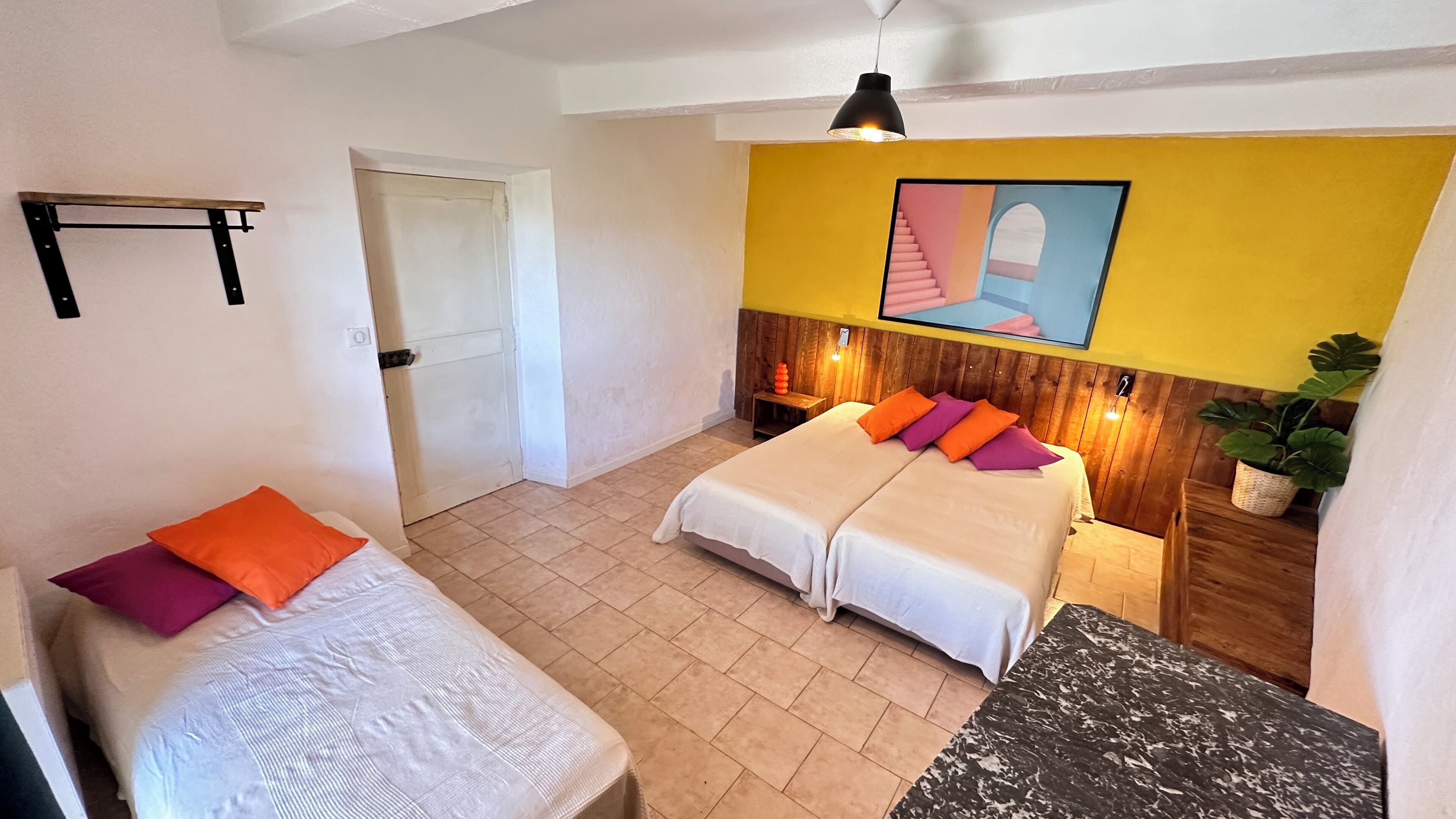 A hotel room with two beds, a wooden headboard, a yellow accent wall, a ceiling fan, and a potted plant.