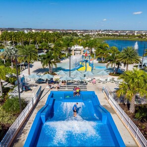 A water park with a large pool, palm trees, and a view of a residential area in the background. - Pool, Spa, Game Room, Theater, 4 Miles to Disney! (Kissimmee)