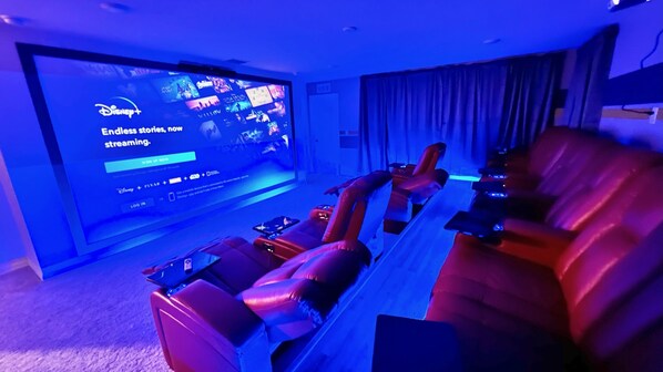 A home theater with a large screen displaying a Disney+ sign-up page, leather reclining chairs, and a carpeted floor. - Pool, Spa, Game Room, Theater, 4 Miles to Disney! (Kissimmee)