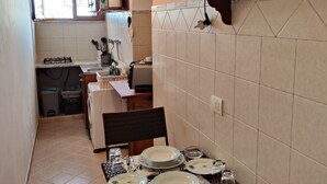 Een kleine keuken met een eethoek voor vier personen. Er is een spoelbak, een fornuis en een raam met uitzicht.