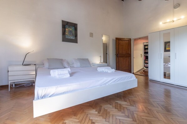 A spacious bedroom with a large bed, a bedside table, a wardrobe, and a wooden herringbone floor. - Italian Experience - Casa Bellavista (Ostra)