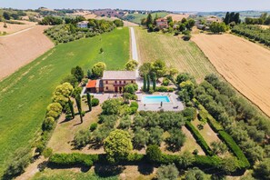 An aerial view of a countryside property with a large house, a swimming pool, and surrounding fields. - Italian Experience - Casa Bellavista (Ostra)