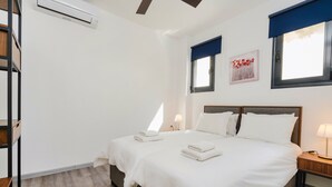 Een hotelkamer met een bed, nachtkastjes, een airconditioner, een raam met een blauwe zonwering en een wandlamp.