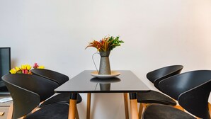 Een moderne eethoek met een zwarte tafel, vier zwarte stoelen, een vaas met bloemen en een klok aan de muur.