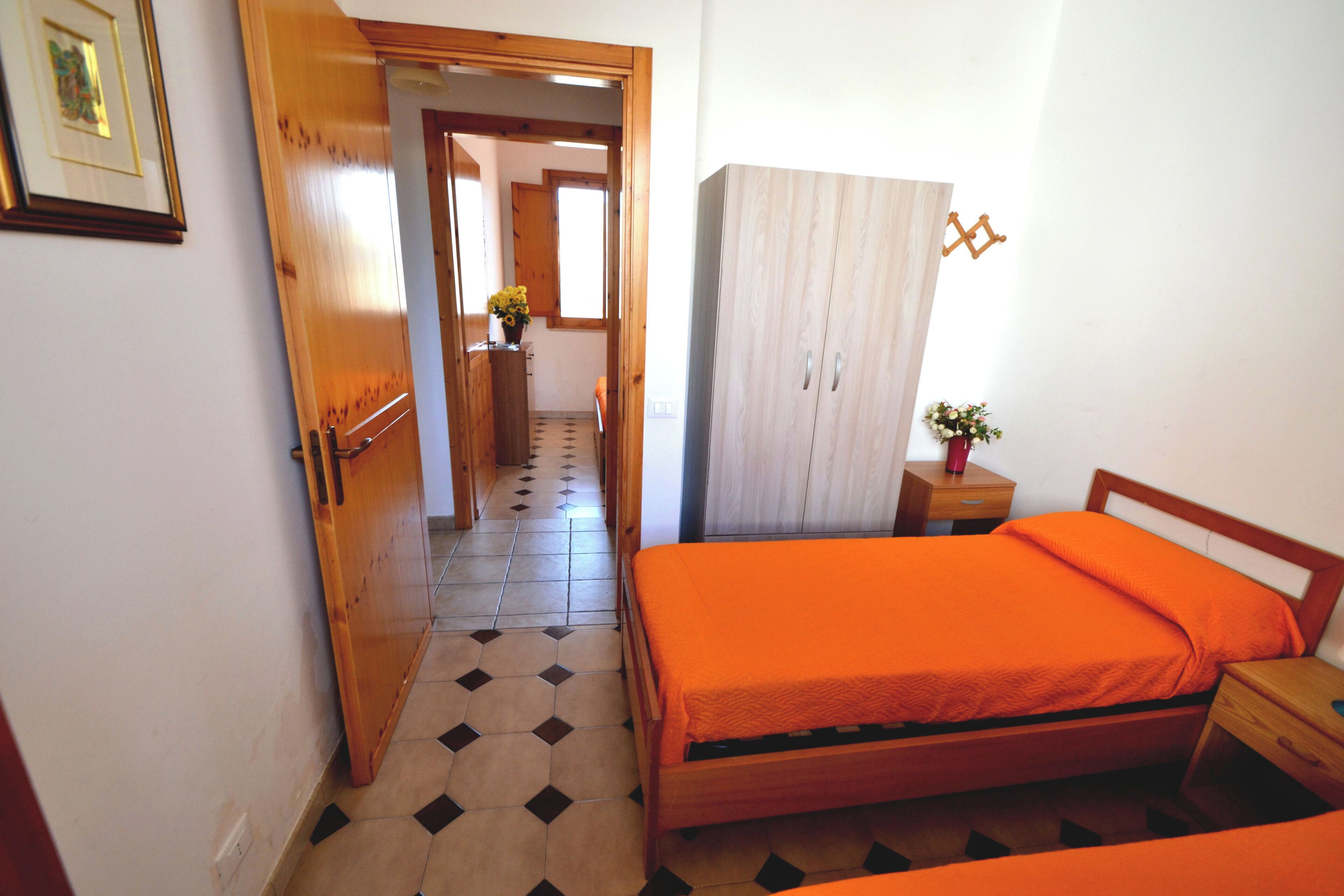A bedroom with a bed, a wardrobe, a nightstand, and a small table with a vase of flowers.