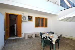 Un patio al aire libre con una mesa, sillas, un banco y una ventana pequeña con persianas.