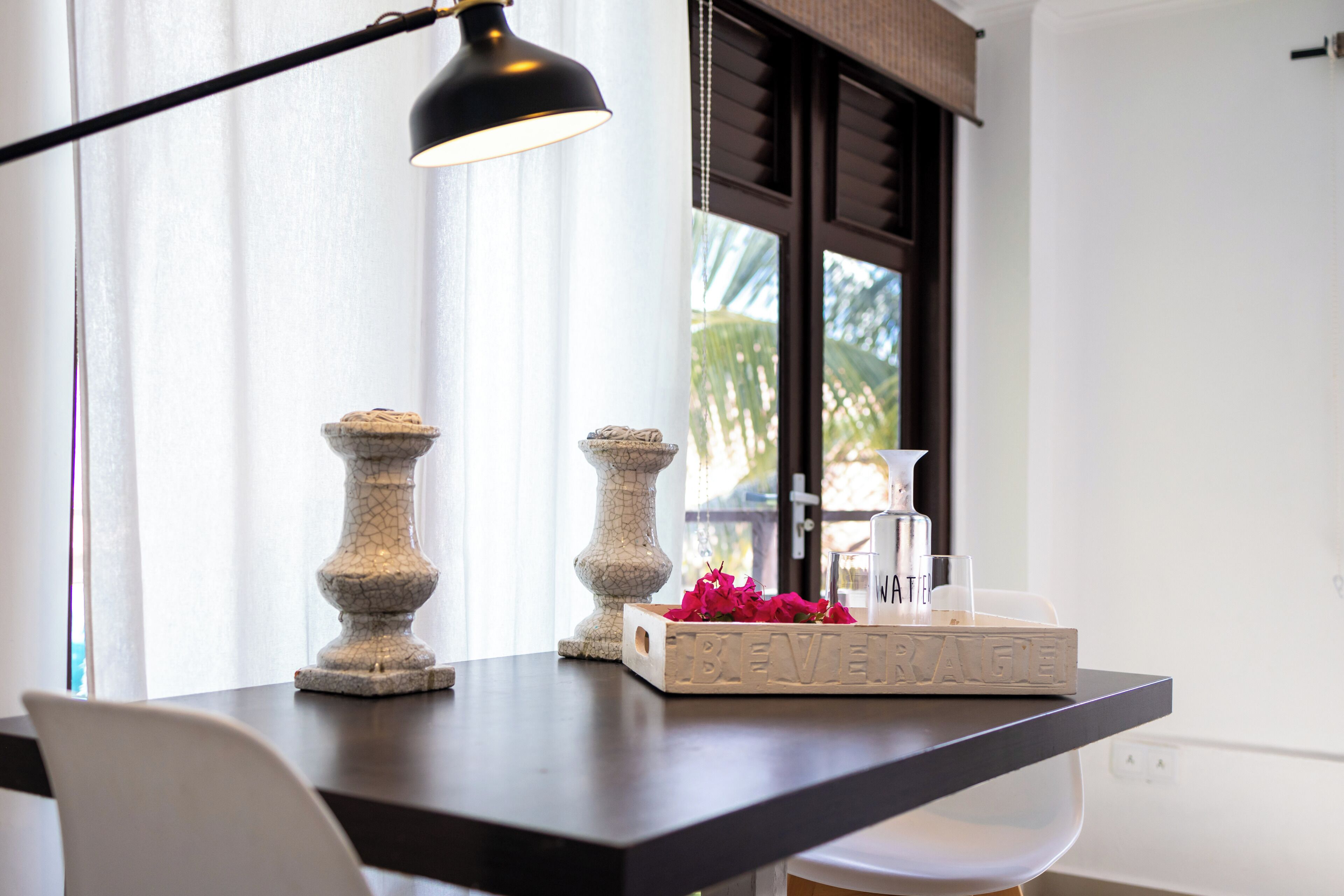 Une table à la surface sombre, deux chandeliers décoratifs, un vase blanc contenant des fleurs roses et une boîte en bois sur laquelle est inscrit le mot «BEVERAGE».