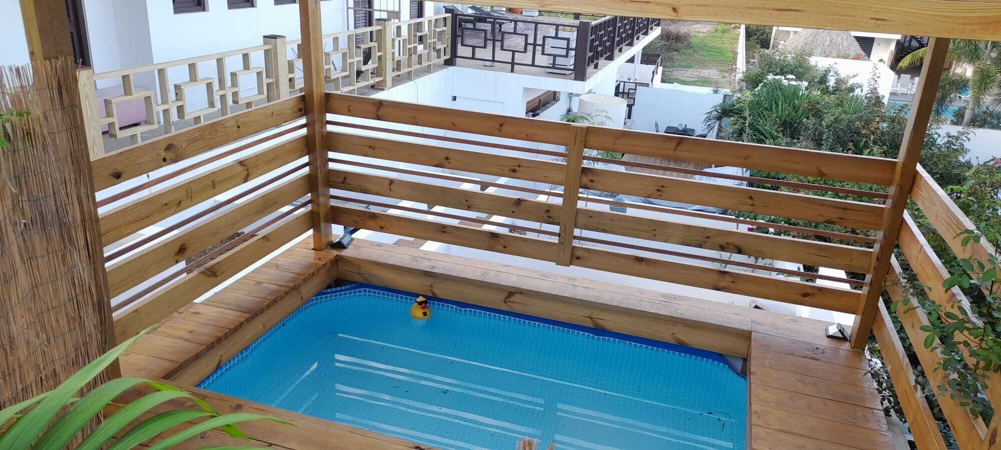 Terraza de madera con piscina, rodeada por un cerco de madera y plantas.