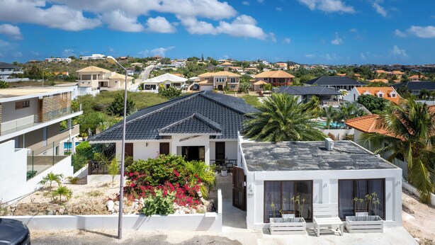 A modern house with a flat roof, a balcony, and a garden with flowering plants. - Apartment With Outside Refreshing Cabin - Mi Cuna Close to Beach (Jan Thiel)
