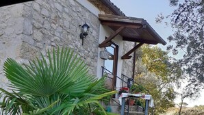 Ein Steinhaus mit einer kleinen Terrasse, einer Palme und einem Tisch mit Blumentöpfen.