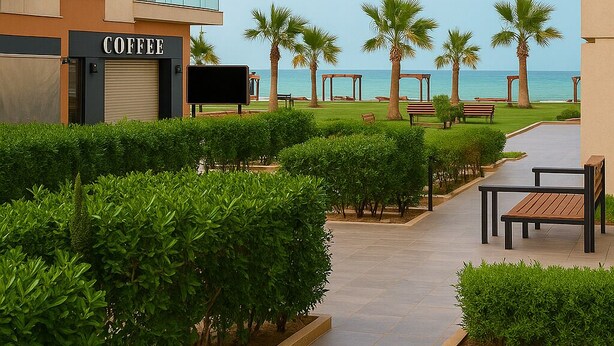 A modern apartment building with a coffee shop on the ground floor, palm trees, and a view of the sea. - Chic Spacious Retreat in Porto Said (Al-Manasrah)