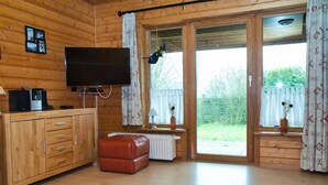 A wooden cabin with a TV, a red leather ottoman, a radiator, and a window with curtains. - House 47 the House to Stay for Holidays (Oberharz am Brocken)