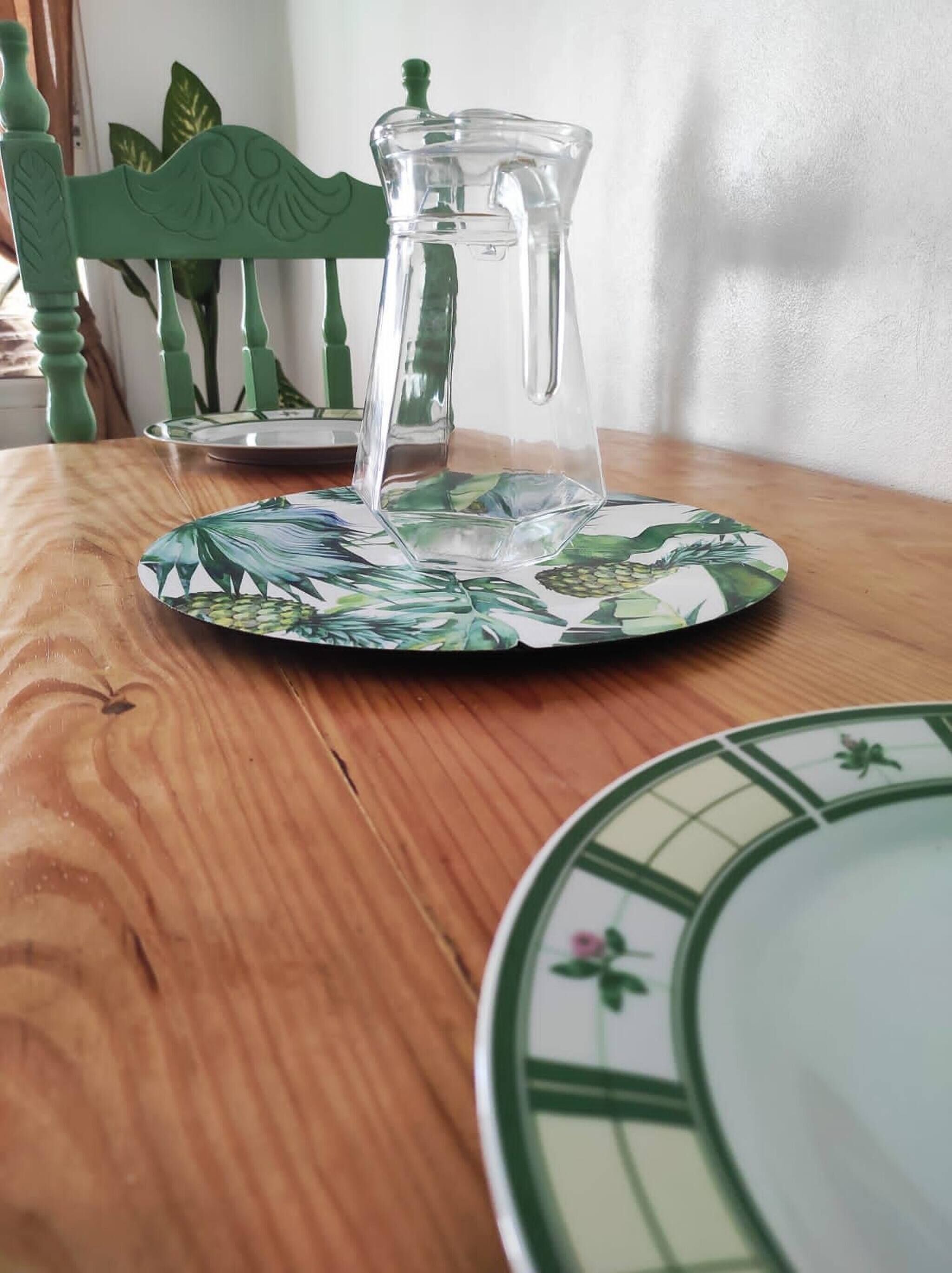 A clear glass pitcher on a table with a tropical leaf pattern plate.