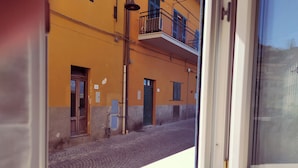 Vista da janela de uma rua com um edifício amarelo, rua de calçada e uma varanda com grade.