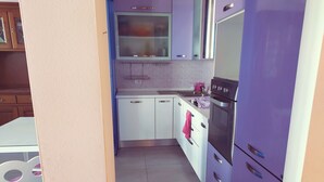 Cozinha com armários brancos, geladeira roxa e painel de azulejos.