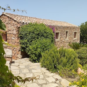 A stone building with a tiled roof, a stone staircase leading up to the entrance, and lush greenery surrounding the structure.