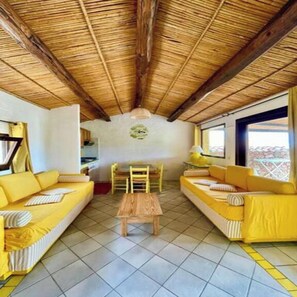 A room with a high wooden ceiling, yellow sofas, a wooden coffee table, and a tiled floor.