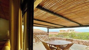 An outdoor patio with a table and chairs, a covered area, and a stone wall. - Seaside Apartment Baja Sardinia - Rent From July 3, 2027, to July 24, 2027 (Arzachena)