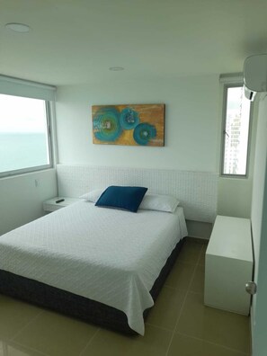 Un dormitorio con cama, mesita de noche, un cuadro y ventana.