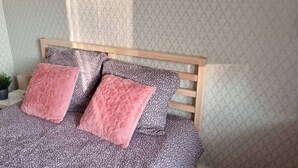 Un lit avec une couvre-lit à motifs floraux, deux oreillers roses, une petite plante en pot et une tête de lit en bois.