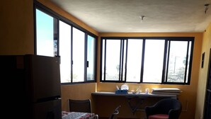 Una habitación con suelo de baldosas, una mesa de comedor con sillas, un refrigerador, un fregadero y ventanas grandes.